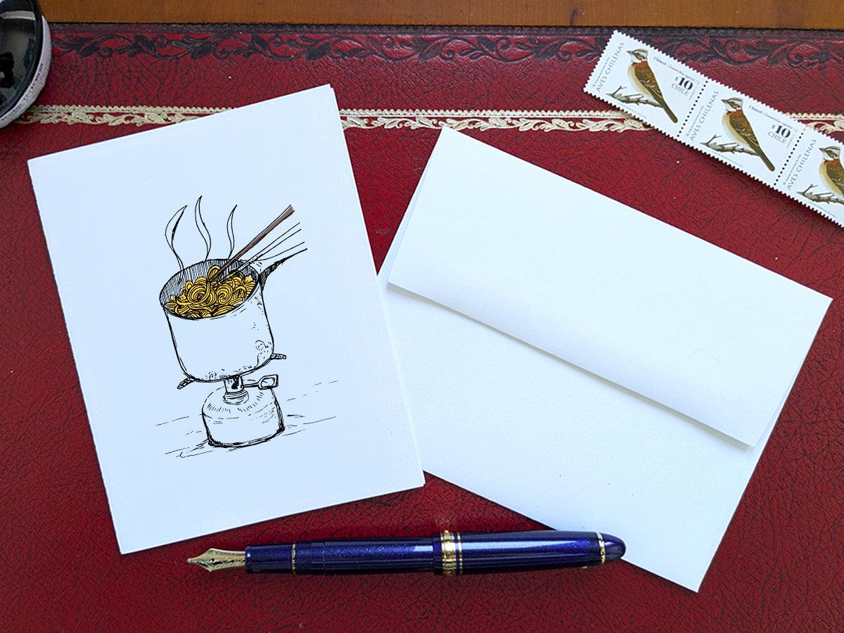 White card with a black ink drawing of a pot of ramen over a camp stove on a red surface with a pen, envelope and stamp.