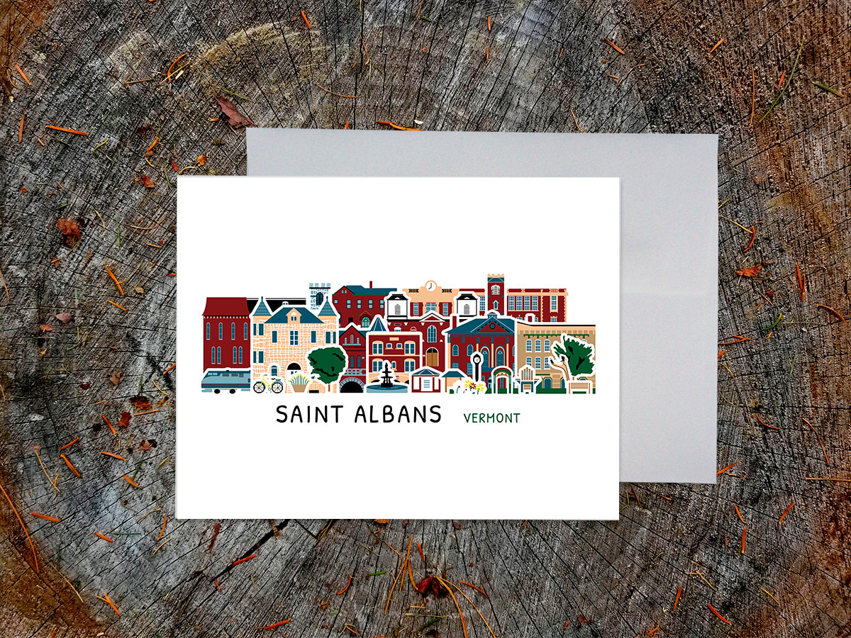 Greeting card with image of buildings arranged in a city skyline with the text Saint Albans Vermont on a table with envelope.