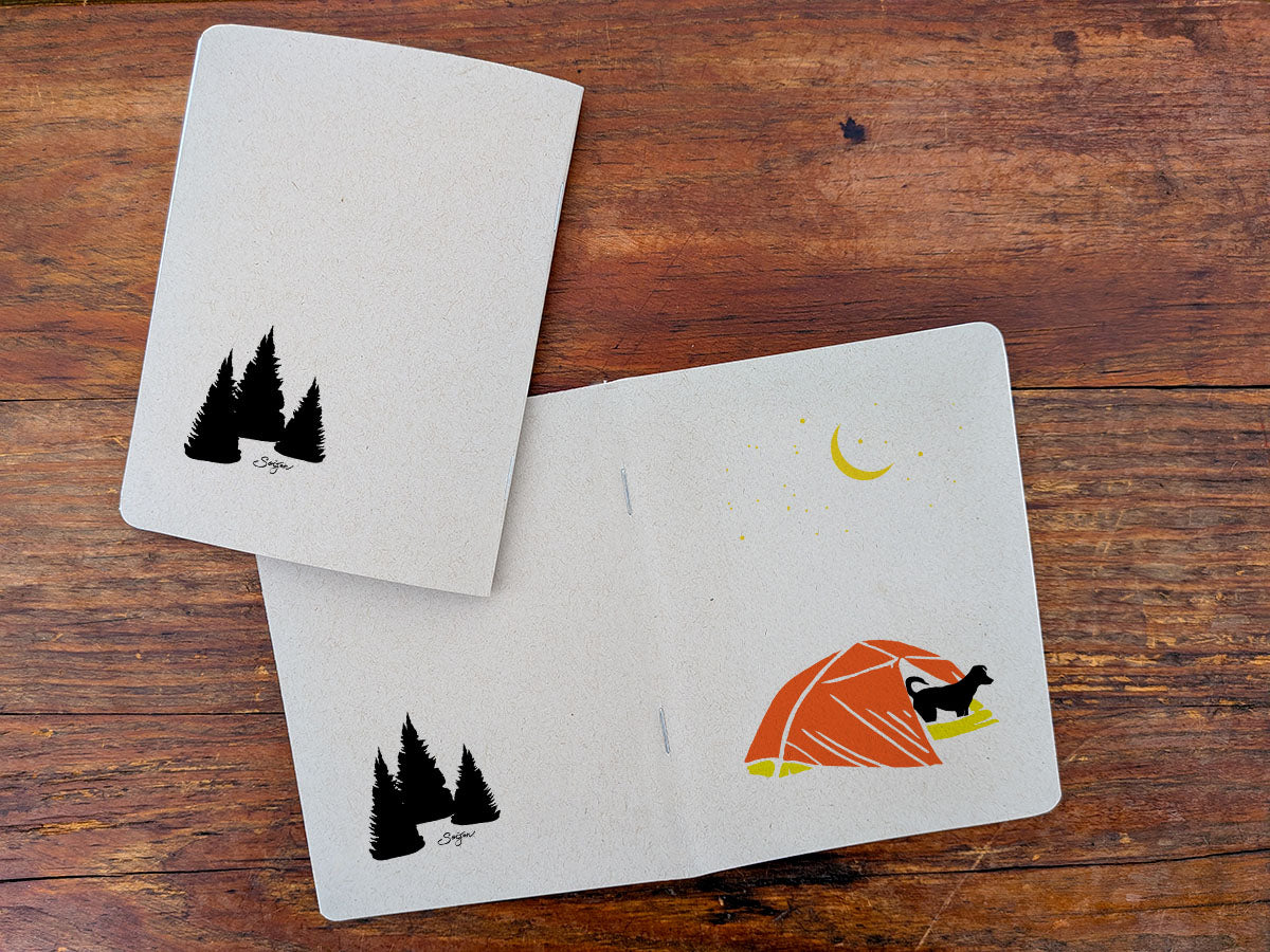 Two notebooks with dog in tent illustration on a wooden surface