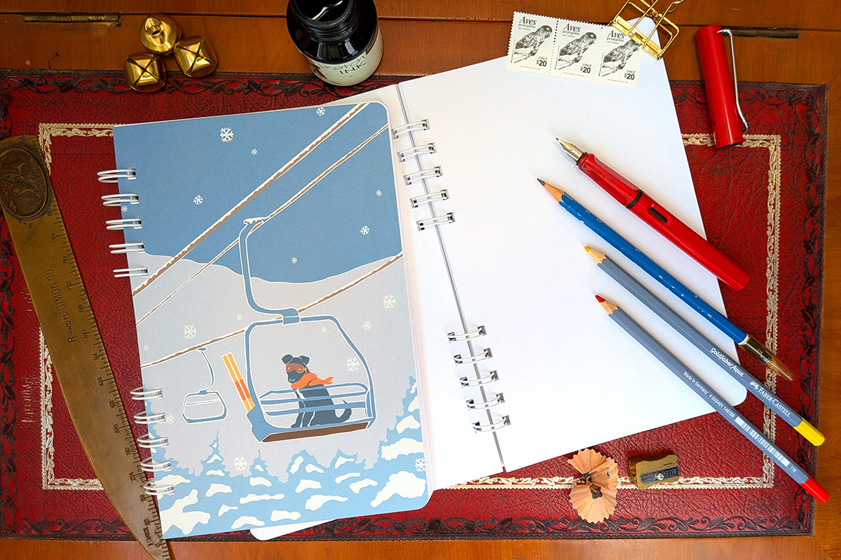 Notebook with illustration of a yellow tent among a background of blue and green mountains.