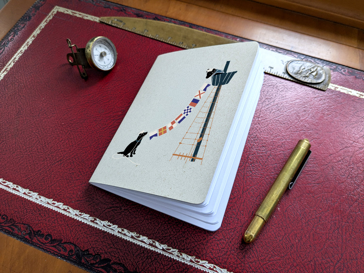 Notebook with two dogs holding nautical flags illustration on a red surface with a pen and small compass.