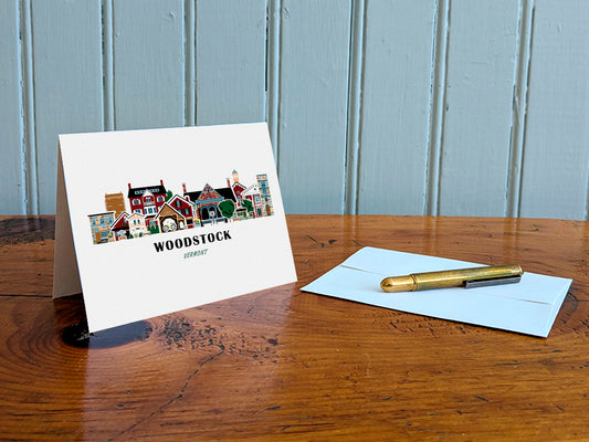 Greeting card with Woodstock, Vermont design on a wooden table with an envelope and pen.