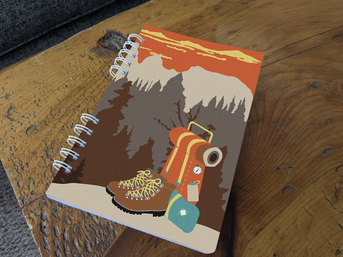 Notebook with illustration of hiking boots and a backpack on table
