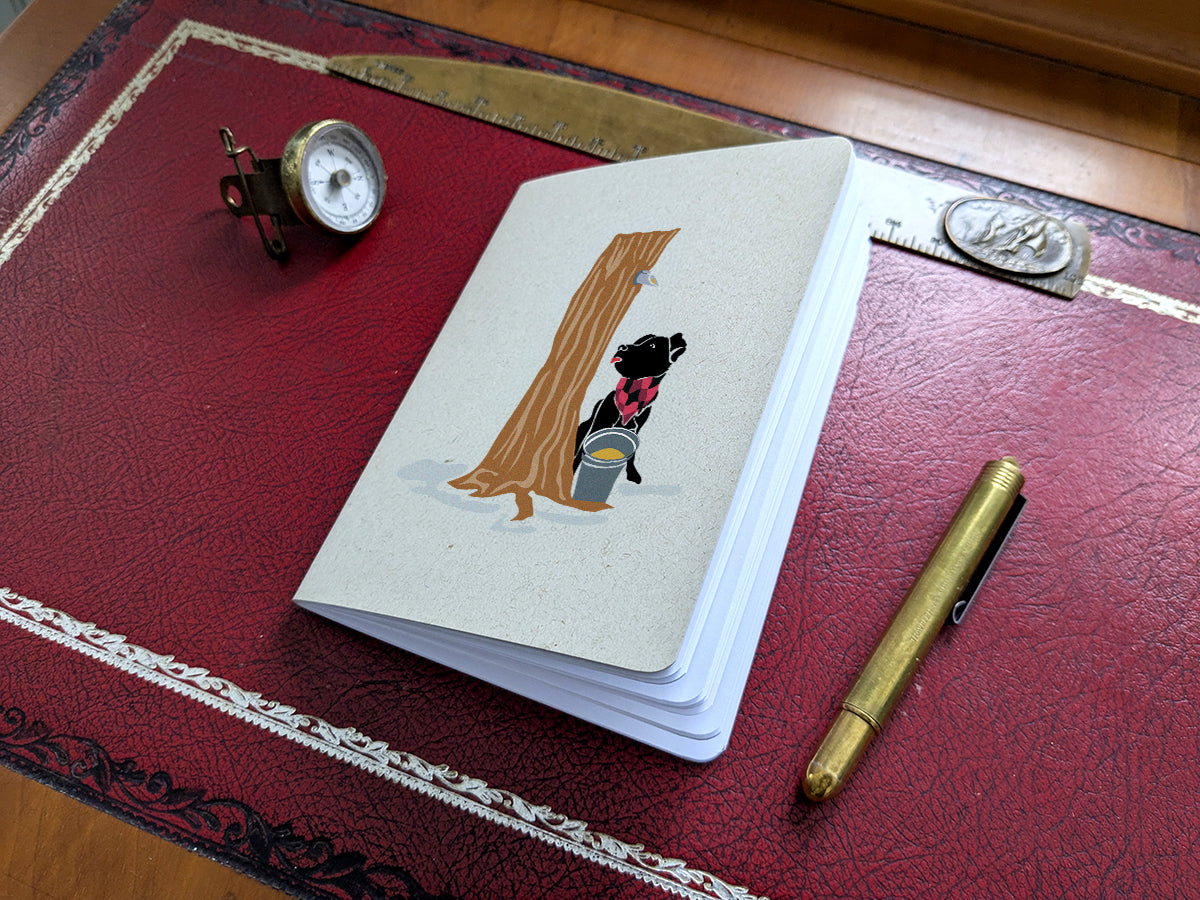 Notebook with dog maple sugaring illustration on a red surface with a pen and small compass.