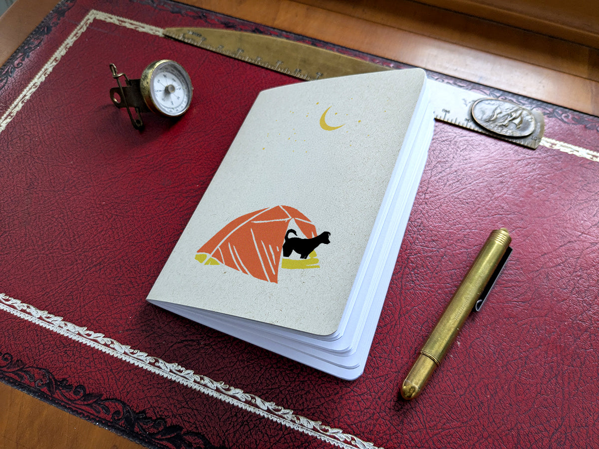 Notebook with dog in a tent illustration on a red surface with a pen and small compass.