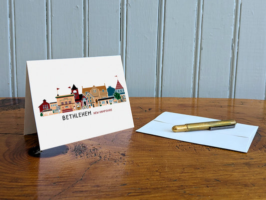 Greeting card with illustration of Bethlehem, New Hampshire, on a wooden table with an envelope and pen.
