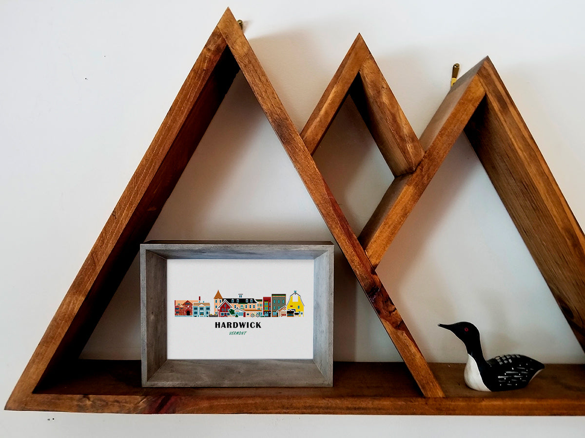 Framed art print on a wooden shelf of buildings arranged in a skyline with the text Hardwick Vermont