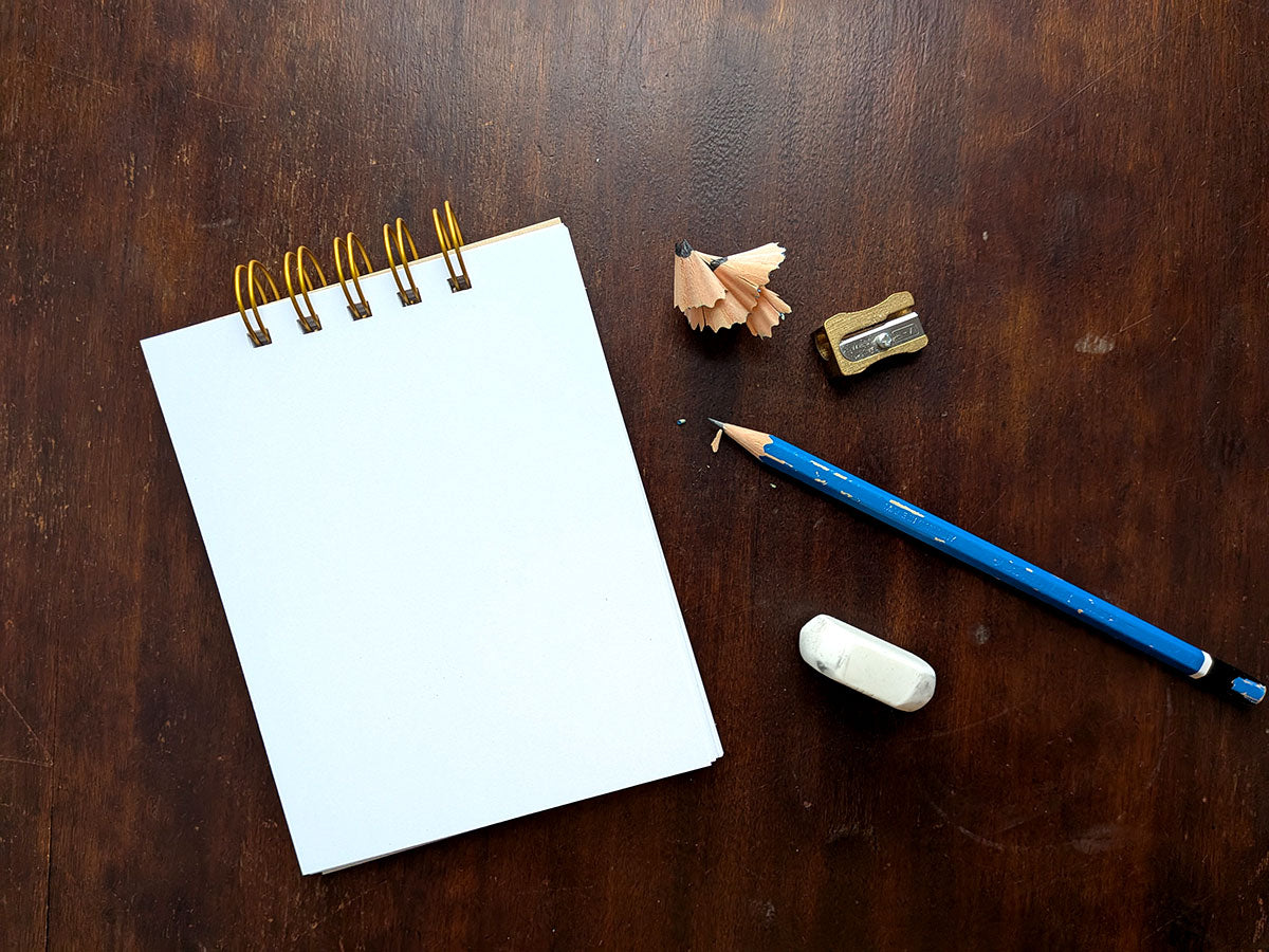 Notebook with a blue pencil, eraser, and sharpener on a wooden surface.