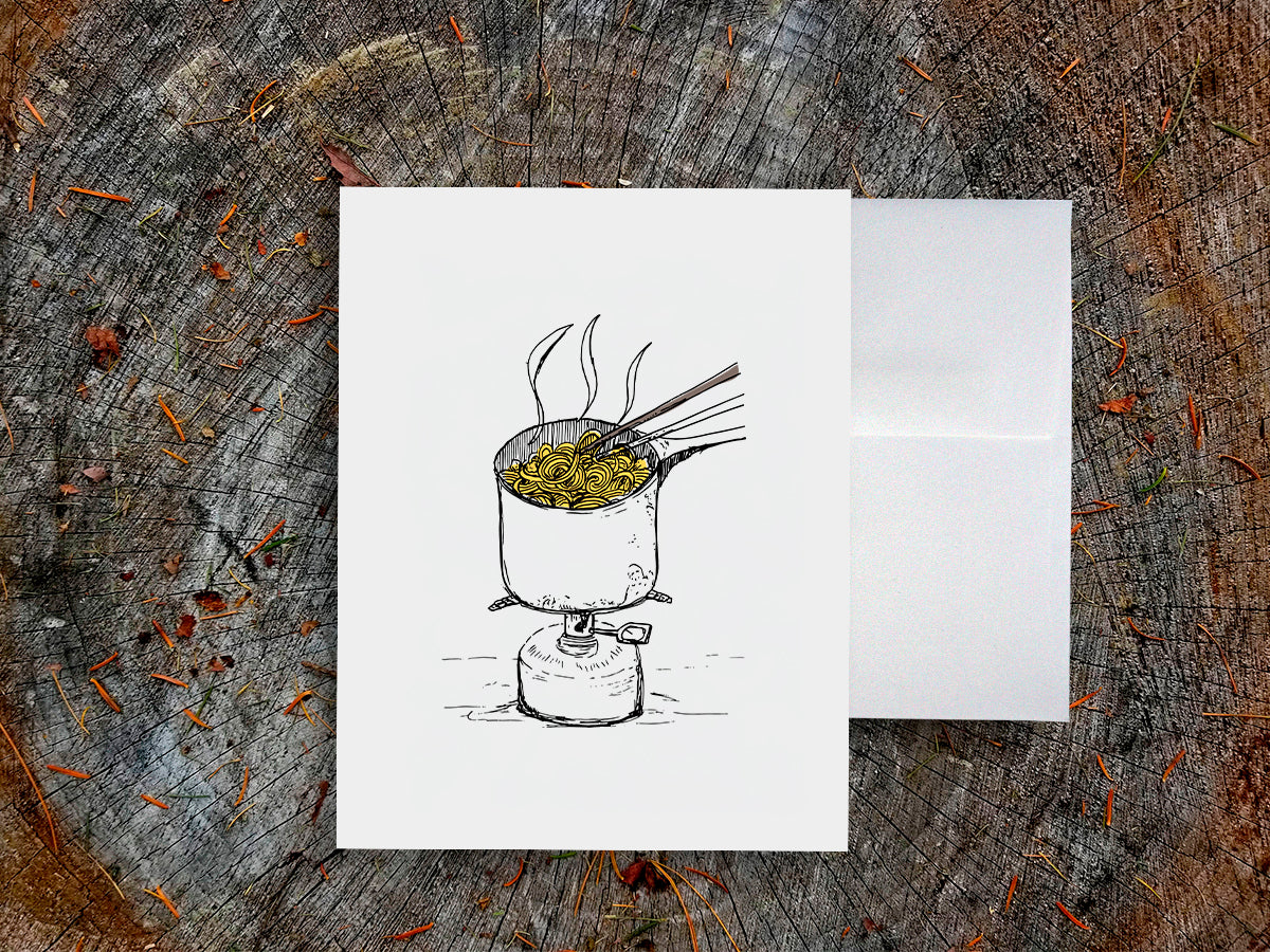 White card with a black ink drawing of a pot of ramen over a camp stove on a wooden surface.