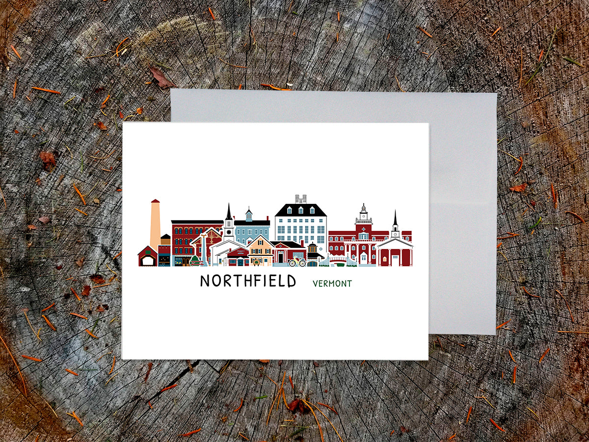 Greeting card with image of buildings arranged in a city skyline with the text Northfield Vermont on a table with envelope.