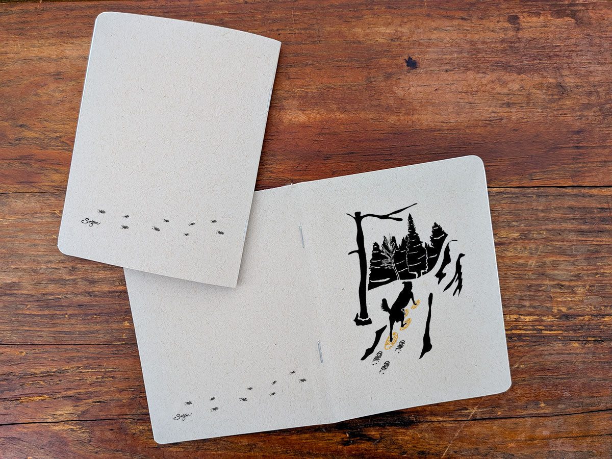 Two notebooks with dog snowshoeing illustration on a wooden surface