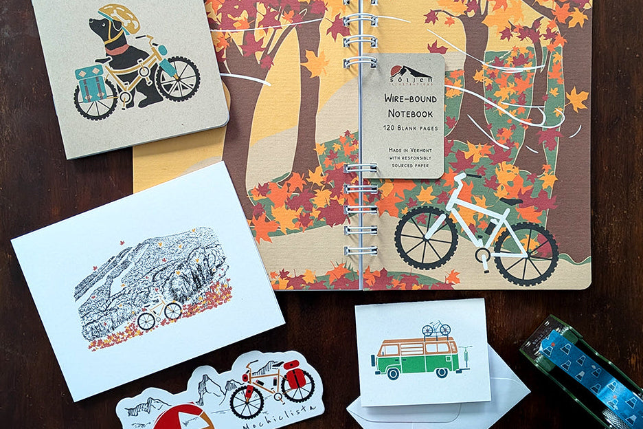 Notebook with autumn biking design, stationery items on a wooden surface